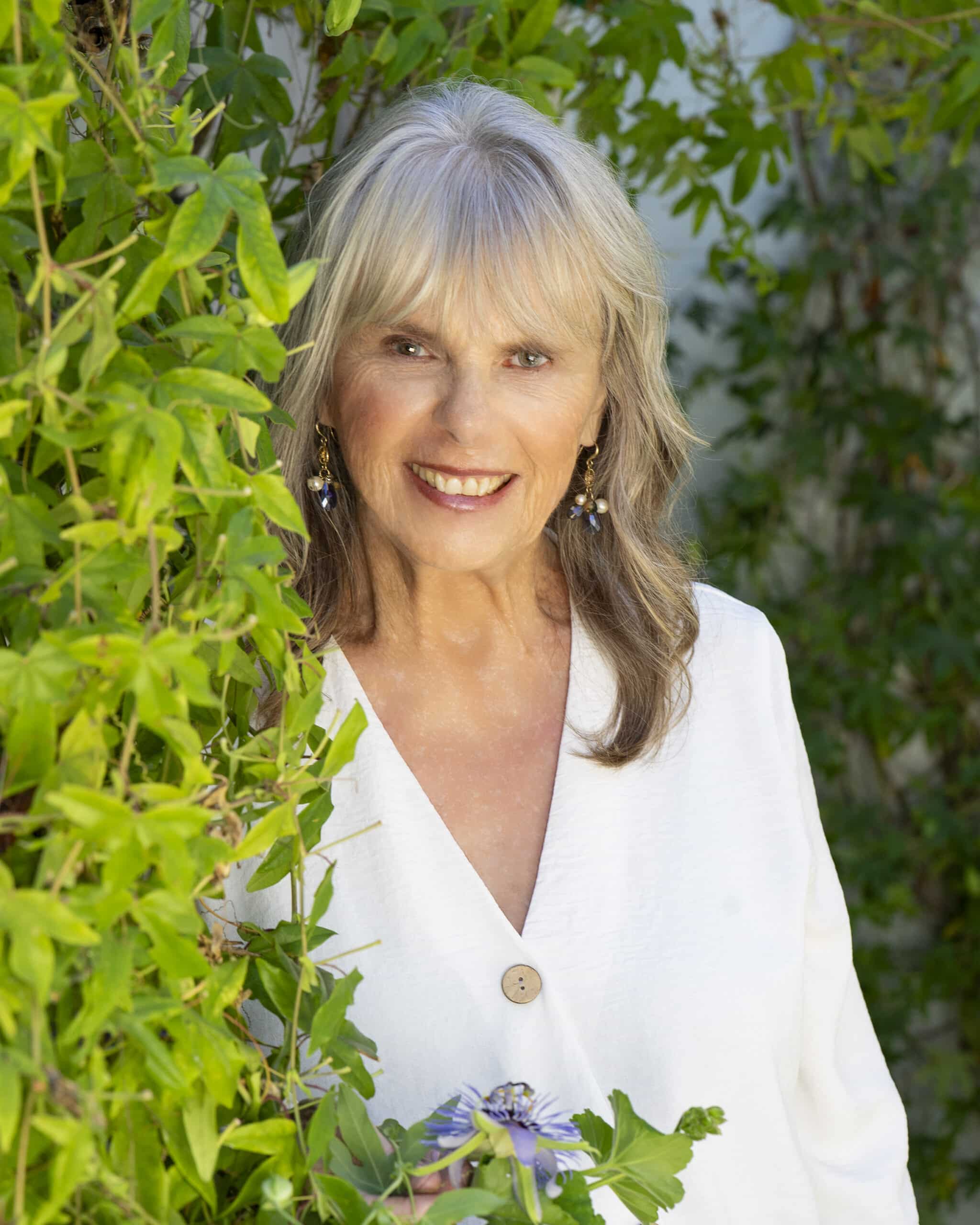 Dr. Susan Allison, Ph.D., in a white linen blouse among green vines