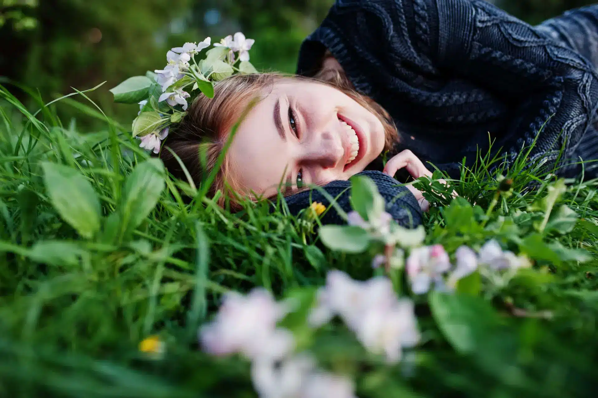 A young woman lying in green grass beneath blossoming branches
