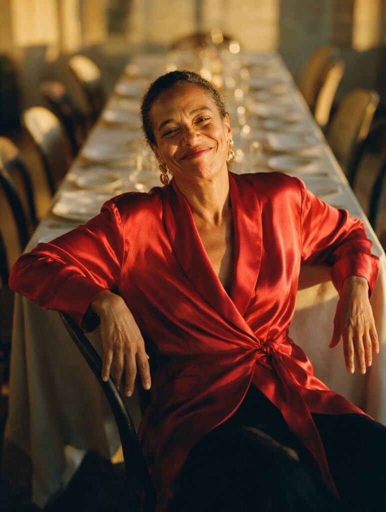 A woman in a red wrap blouse leaning back in her chair at a long candlelit table