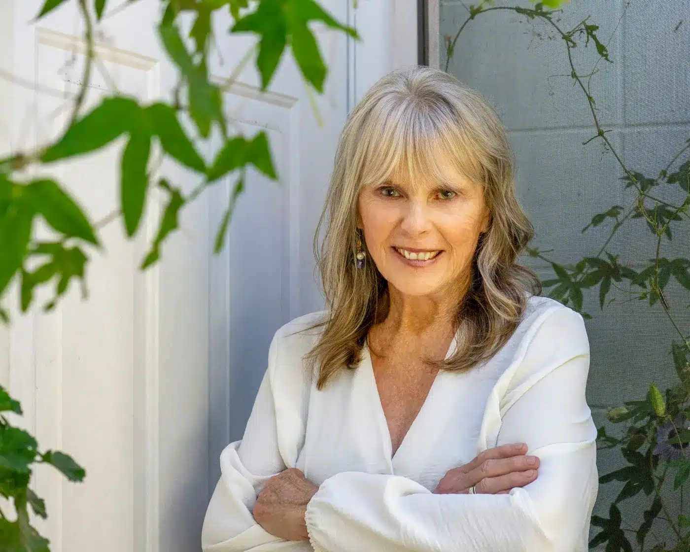 Dr. Susan Allison, Ph.D., in a white linen blouse with arms folded, among green vines