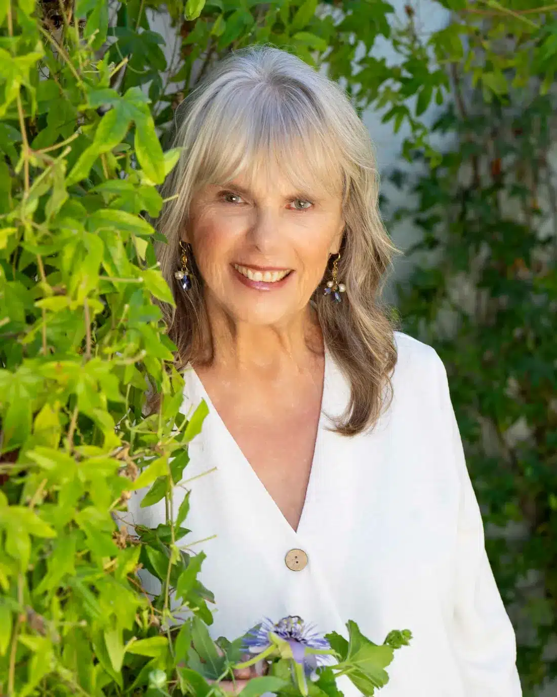 Dr. Susan Allison, Ph.D., in a white linen blouse among green vines